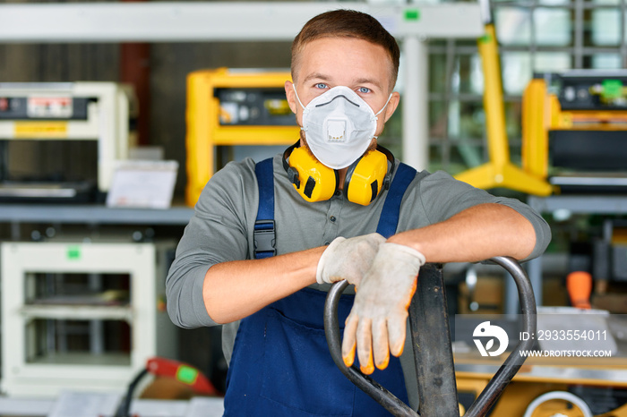 Portrait of cheerful young worker wearing protective mask posing looking at camera and enjoying work at modern factory