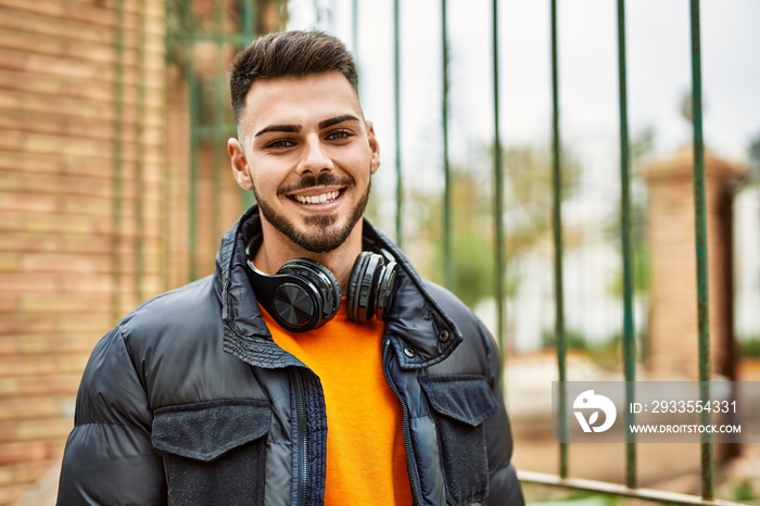 Handsome hispanic man with beard smiling happy and confident at the city wearing winter coat and headphones