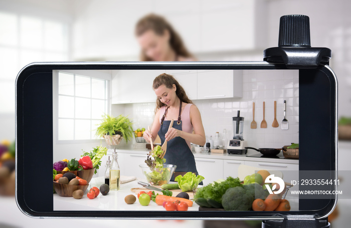 Young female blogger and vlogger and online influencer live streaming a cooking show on social media using a smartphone