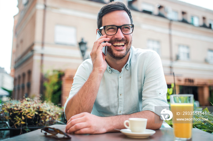 Happy young man sitting in the cafe, drinking coffee and making a phone call. Lifestyle concept