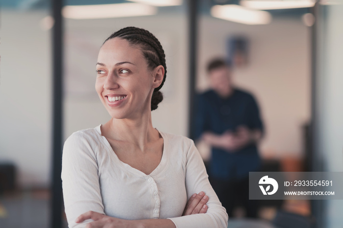 Portrait of young smiling business woman in creative open space coworking startup office. Successful businesswoman standing in office with copyspace. Coworkers working in background.