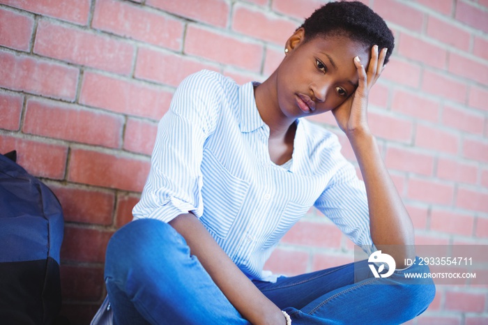 Sad schoolgirl sitting against brick wall