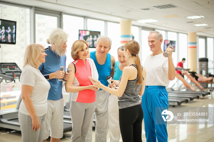 Group of elderly people and trainer with phone in gym