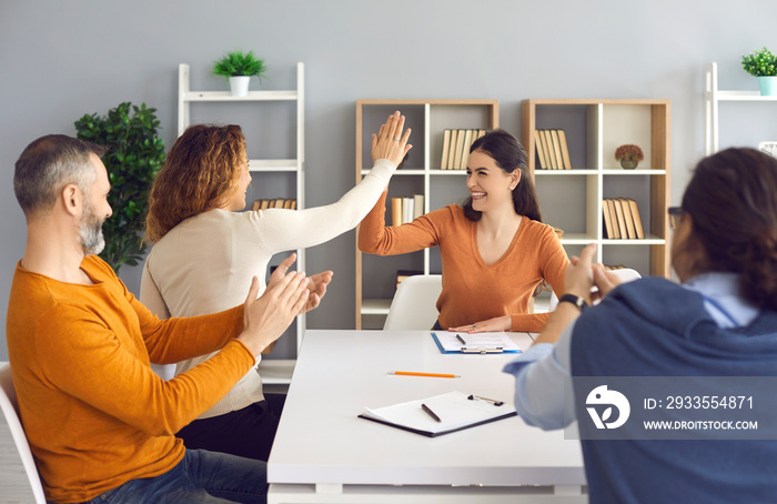 Happy professional business teams making successful deal. Group leaders celebrating success and teamwork. Two smiling women entrepreneurs high fiving each other sitting at office table in work meeting