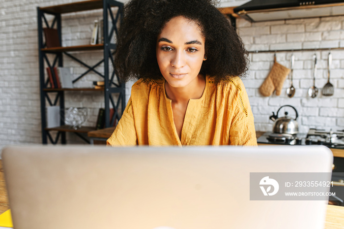 Close-up portrait of concentrated african woman uses laptop for work from home. A girl with an afro hairstyle focused on screen