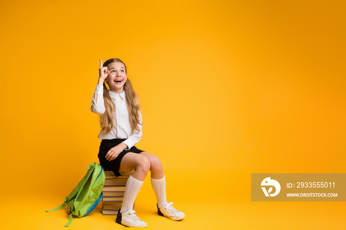 Clever Elementary School Girl Pointing Finger Up Sitting On Stack Of Books