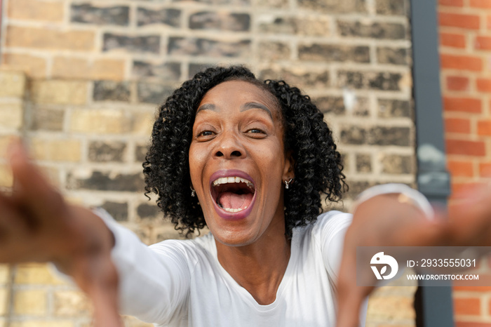 Portrait of woman reaching hands against brick wall