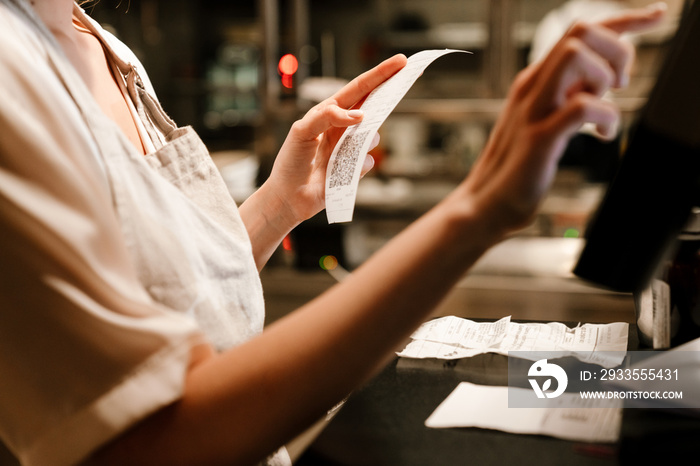 Young woman holding order receipts while working in restaurant kitchen