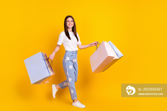 Full size profile side photo of happy positive girl shopaholic hold shopping bags isolated on yellow color background