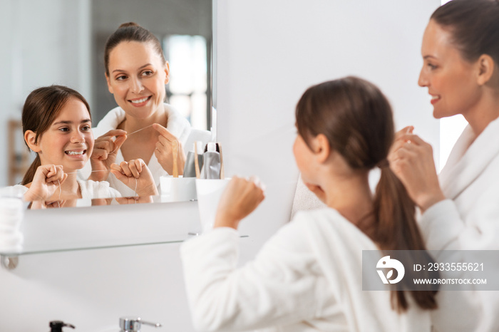 beauty, hygiene, morning and people concept - happy smiling mother and daughter with dental floss cleaning teeth and looking to mirror at bathroom