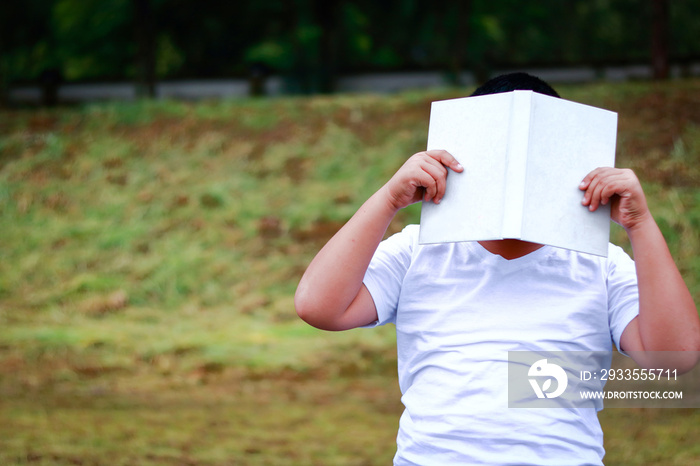 Asian boy holding a white book off his face