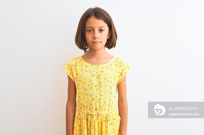 Young beautiful child girl wearing yellow floral dress standing over isolated white background Relaxed with serious expression on face. Simple and natural looking at the camera.