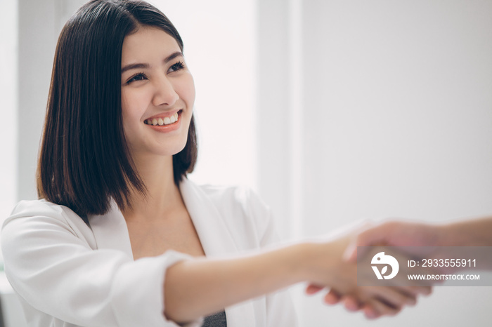 Beautiful young asian business woman smiling with triumphant of the success deal or project while shaking hand with business man with the white natural sunlight as a background.