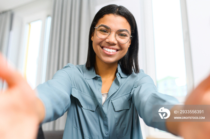 Waist up portrait view of the brunette girl wearing glasses making selfie with toothy smile or calling to friend via video call. Internet connection concept