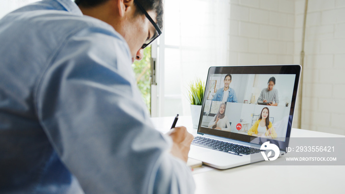 Young Asia businessman using laptop talk to colleagues about plan in video call meeting while work from home at living room. Self-isolation, social distancing, quarantine for corona virus prevention.