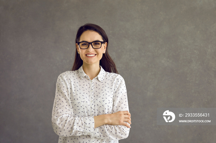 Happy confident smiling caucasian woman looking at camera studio headshot portrait. Casual positive lady showing cheerful emotion sanding on grey background. Feminine and youth, people expression