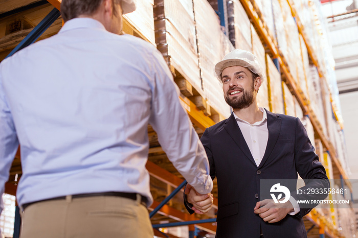 Business meeting. Pleasant nice businessmen shaking hands while meeting each other in the storehouse