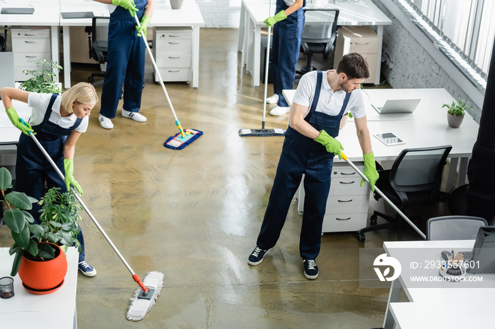 High angle view of cleaners washing floor near tables in office