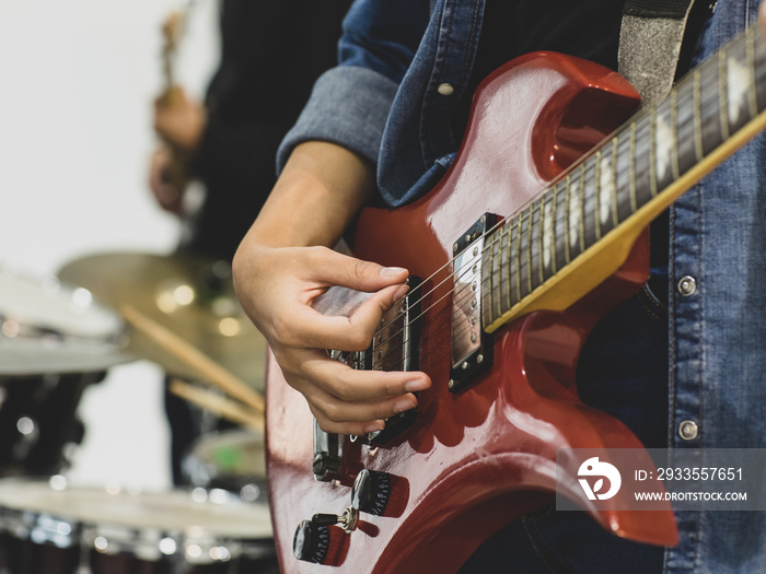 Close-up shot of young female musician hands playing the electric guitar. Selective focus on the guitarist’s hands with a drum in the background. Guitarist playing music together with a classmate