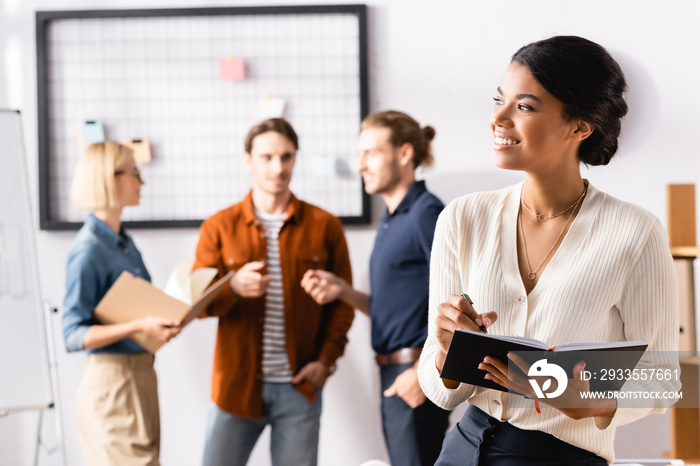 happy african american businesswoman looking away while multicultural colleagues communicating on blurred background