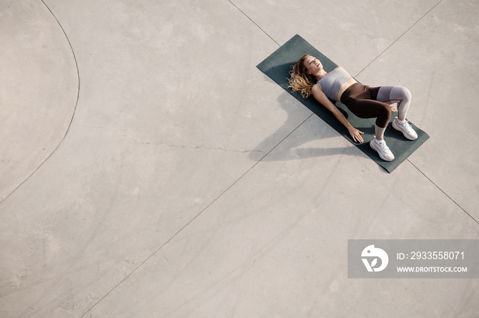 Young fitness woman stretching back while laying at the yoga mat