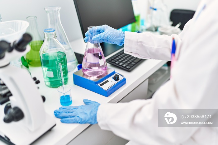 Young hispanic woman wearing scientist uniform measuring test tube at laboratory