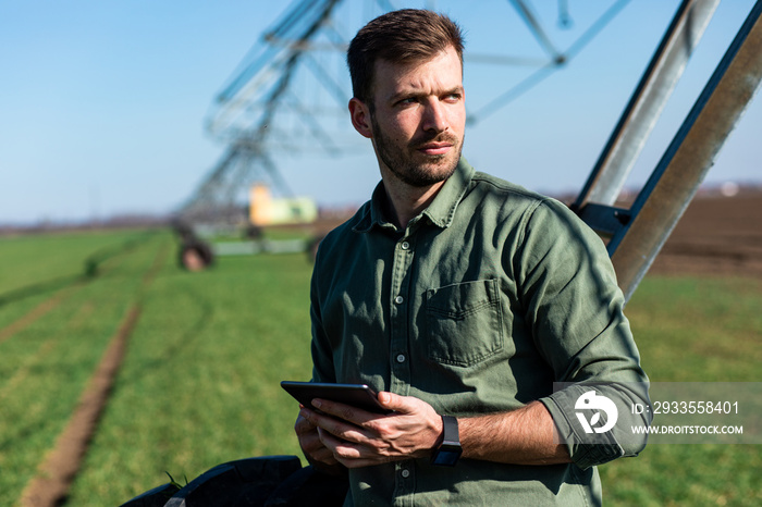 Young farmer standing in wheat field and setup irrigation system on tablet.