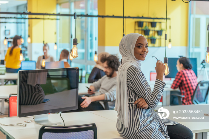 Protrait of a black ( african-american) female muslim standing in a modern business office while wearing a hijab.