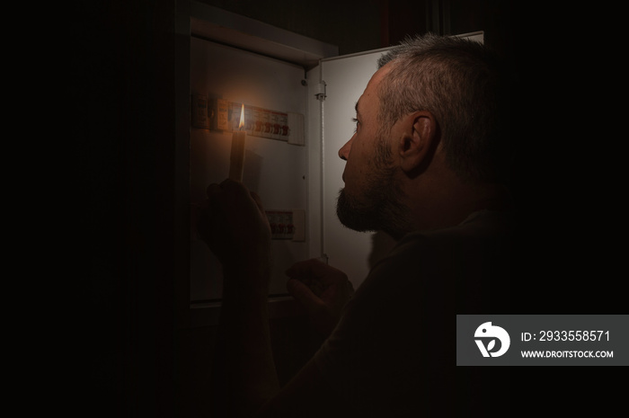 Blackout, No electricity. A man with a candle in the dark examines the electrical switchboard at home.