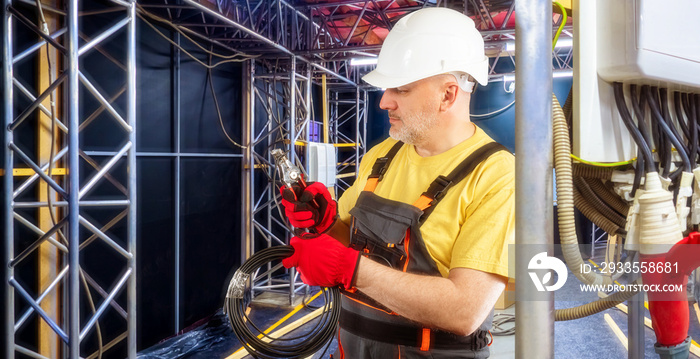 Connecting electrical equipment. Electrician man makes wiring before concert. Engineer in helmet and overalls. Man on temporary stage sets up wires. Electrician with wires. Concert preparation