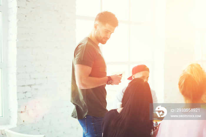 Bearded handsome male member of skilled team talking with female colleagues and discussing general work concepts in sunshine studio.Good looking man sharing experience and giving advices for partner