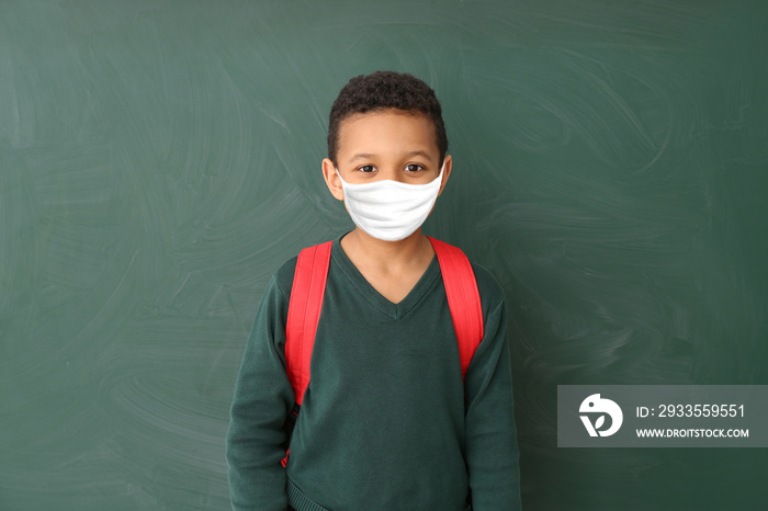 Cute African-American schoolboy wearing protective mask in classroom. Concept of epidemic