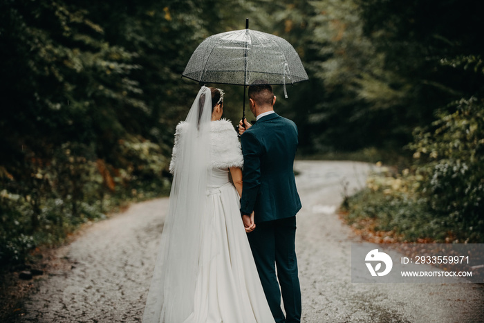 Wedding happy moments. Happy young couple, newlyweds walking the streets in rainy weather while carrying an umbrella.