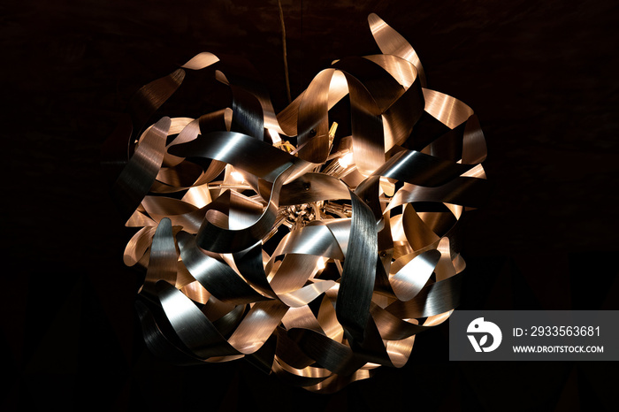 Metal ribbon chandelier closeup. Modern lampshade. Copper and silver textured background. Abstract chaotic pattern. Futuristic abstract backdrop in shades of bronze