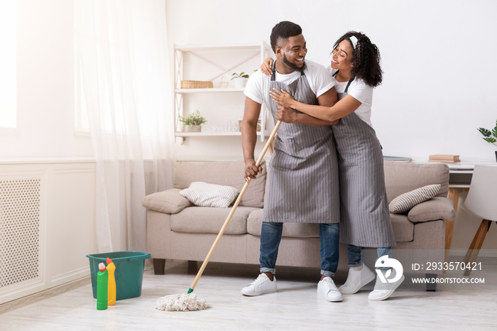 Happy black couple doing household chores together, mopping floor and hugging