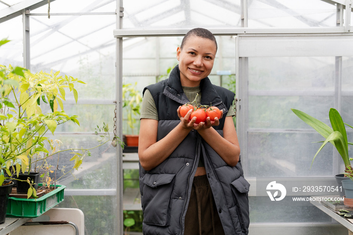 Portrait of smiling woman holding tomatoes in greenhouse