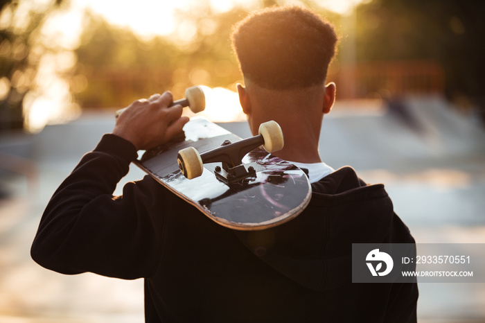 Back view of a male teenager guy holding skateboard