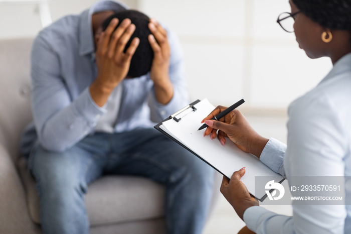 Depressed black guy holding his head at counselor’s office, seeking professional help with mental disorder