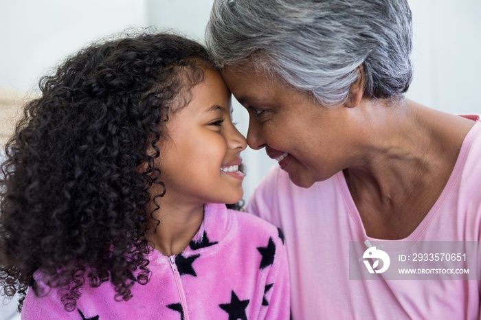 Smiling granddaughter and grandmother sitting face to face in bed