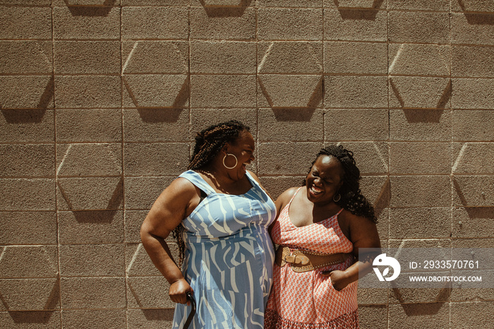 2 plus size African American women stand against a wall laughing