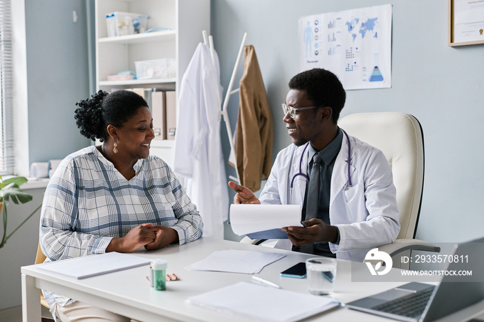 Young black doctor talking to young woman during consultation in clinic smiling