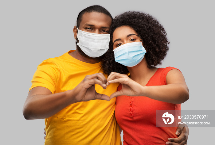 health, quarantine and pandemic concept - happy african american couple wearing protective medical masks for protection from virus making hand heart gesture over grey background