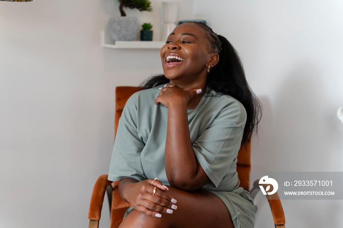 Portrait of young woman laughing while sitting in armchair at home