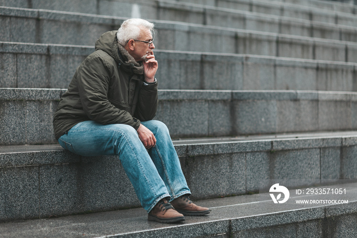 Gray-haired man is lost in thought and sits on the steps. Nostalgia for a pensioner.