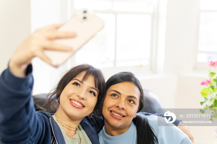 Two women sitting on sofa and using smartphone to take selfie