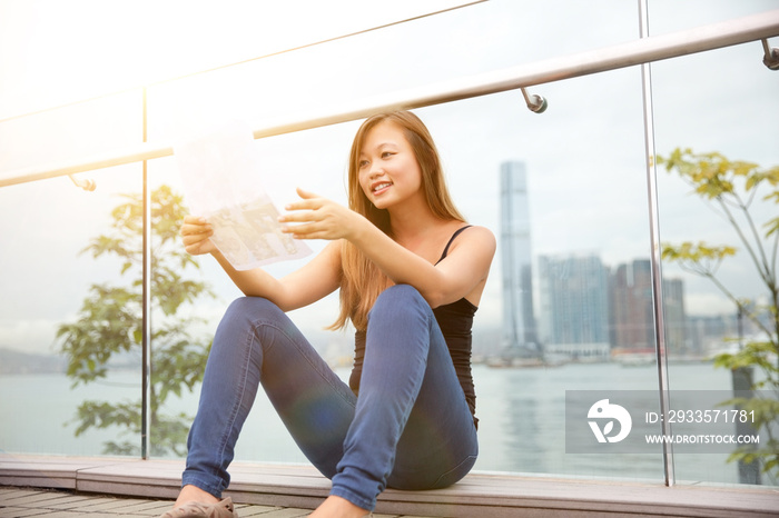 Young woman sitting beside harbour, Hong Kong, China