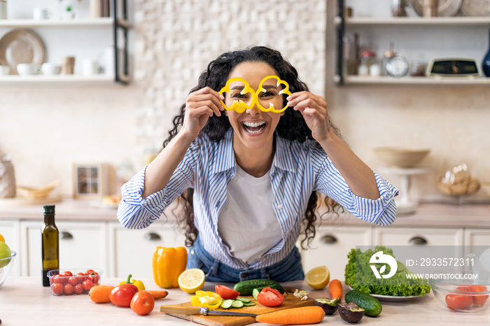 Excited woman making glasses of sweet pepper, having fun and playing with food while cooking fresh salad