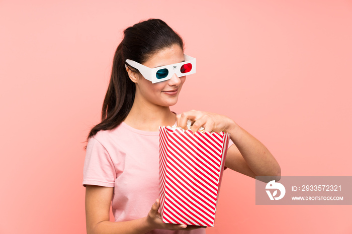 Teenager girl over isolated pink wall eating popcorns with 3d glasses