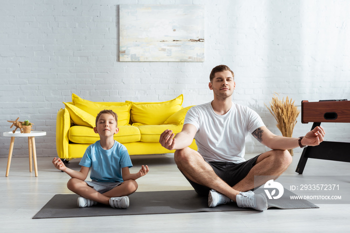 father and son sitting in lotus poses on fitness mat with closed eyes