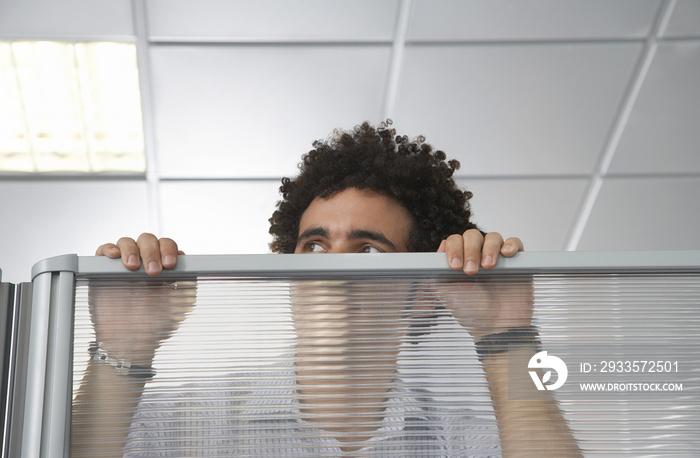 Young male office worker peering over cubicle wall in the office